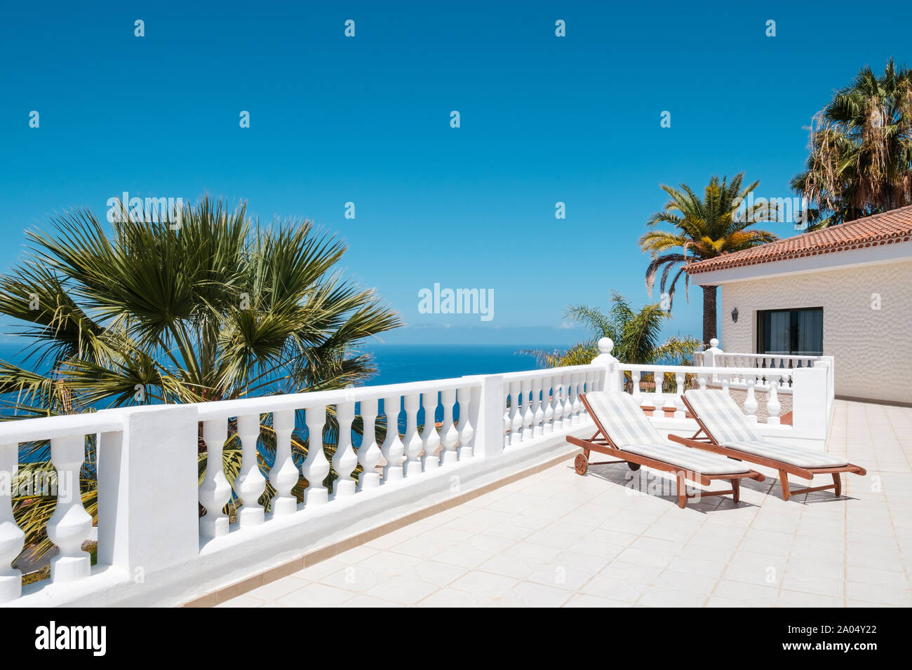 Terrasse ensoleillée avec des chaises longues de ocean view house avec palmiers et ciel bleu copy space Banque D'Images