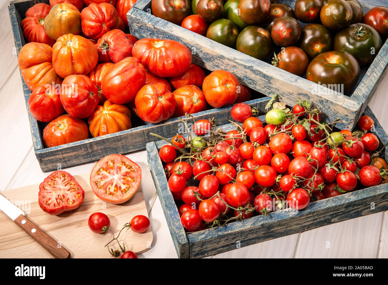 Variété de tomates fraîches dans des caisses sur fond de bois. Raf, tomates kumato et cerise. Banque D'Images