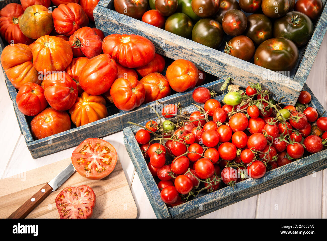 Variété de tomates fraîches dans des caisses sur fond de bois. Raf, tomates kumato et cerise. Banque D'Images