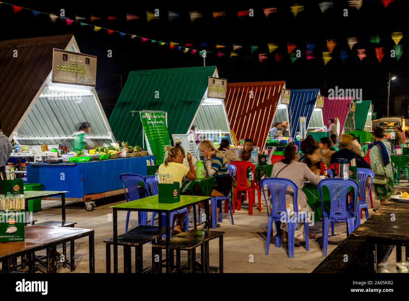 La population locale et les touristes de manger des aliments de rue à des tables dans le marché de nuit, Nyaung Shwe, le lac Inle, l'État de Shan, Myanmar. Banque D'Images
