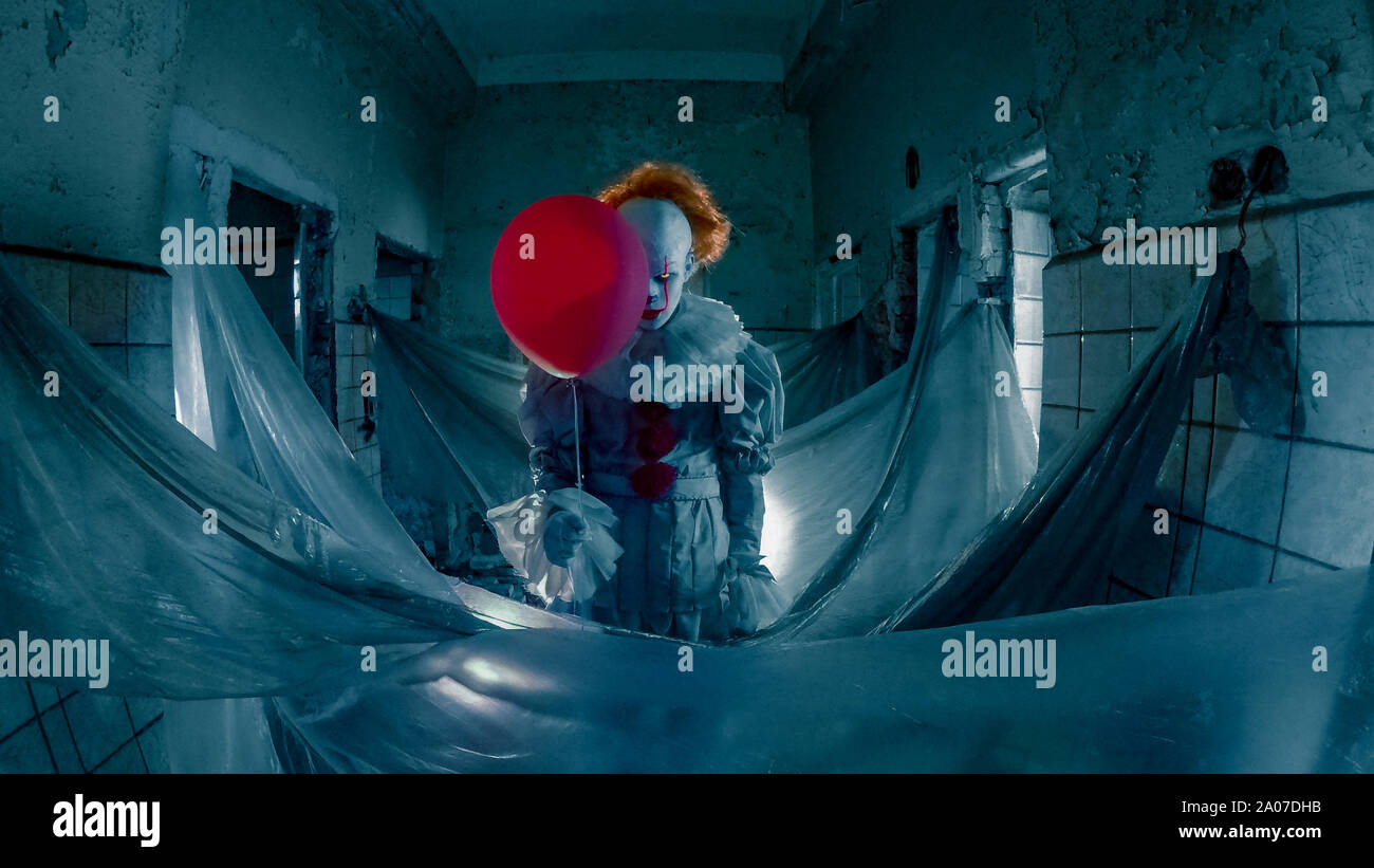 Un homme à l'image de clown au ballon rouge dans sa main se trouve dans le vieux bâtiment abandonné. Banque D'Images