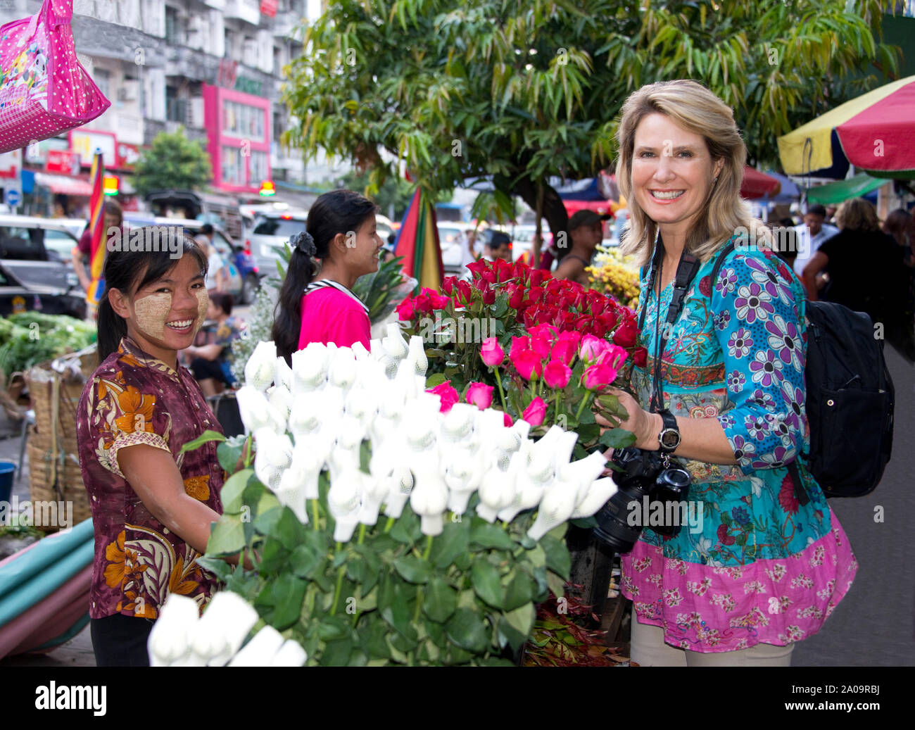 Caucasian Woman qui est publiée et un modèle femme birmane traditionnelle avec du vendeur Maquillage Thanaka Vente de fleurs à l'extérieur de la rue du Marché Banque D'Images