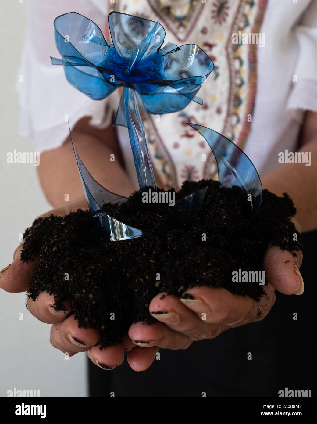 Mains d'une vieille femme tenant une fleur en plastique bleu et le sol naturel. L'expression de l'image conceptuelle d'alarme mondiale sur le changement climatique. Banque D'Images