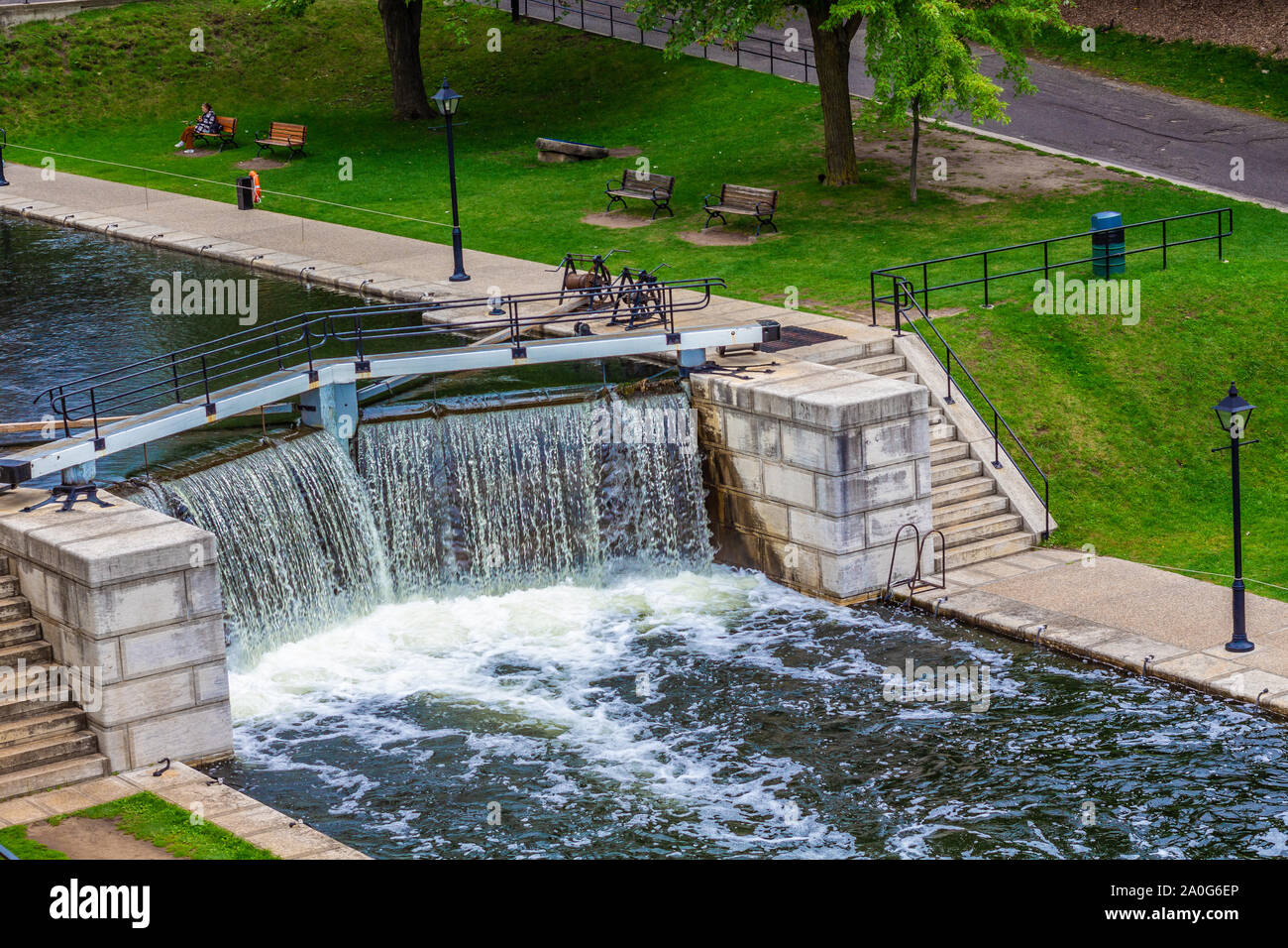 L'eau coule sur le bord d'un verrou dans un canal. Escaliers et murs en pierre les verrous de ligne, qui sont entourées d'un parc public. Banque D'Images