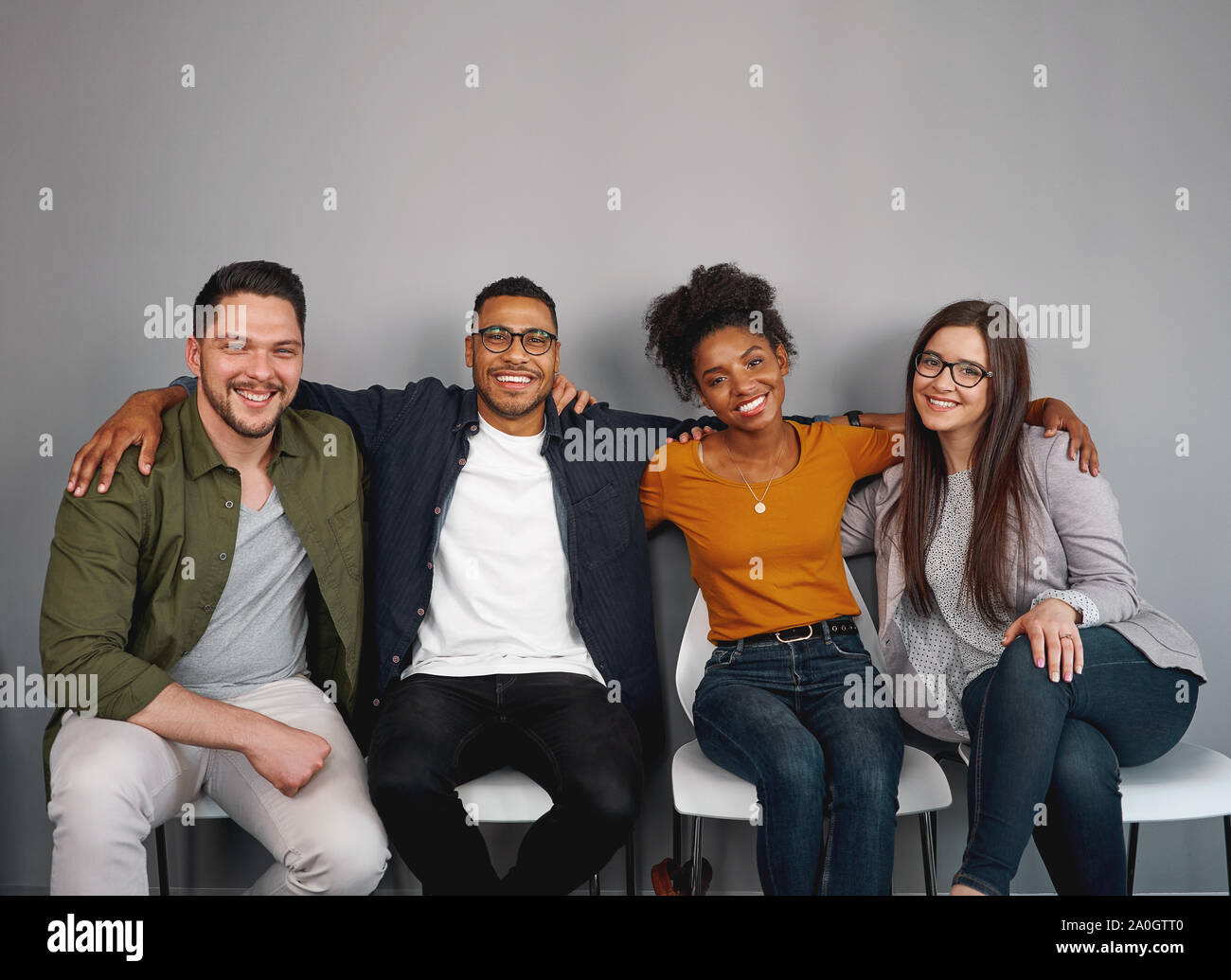 Portrait de jeunes amis multiethnique siégeant ensemble heureux avec leurs bras autour de l'autre sur une chaise smiling and looking at camera Banque D'Images