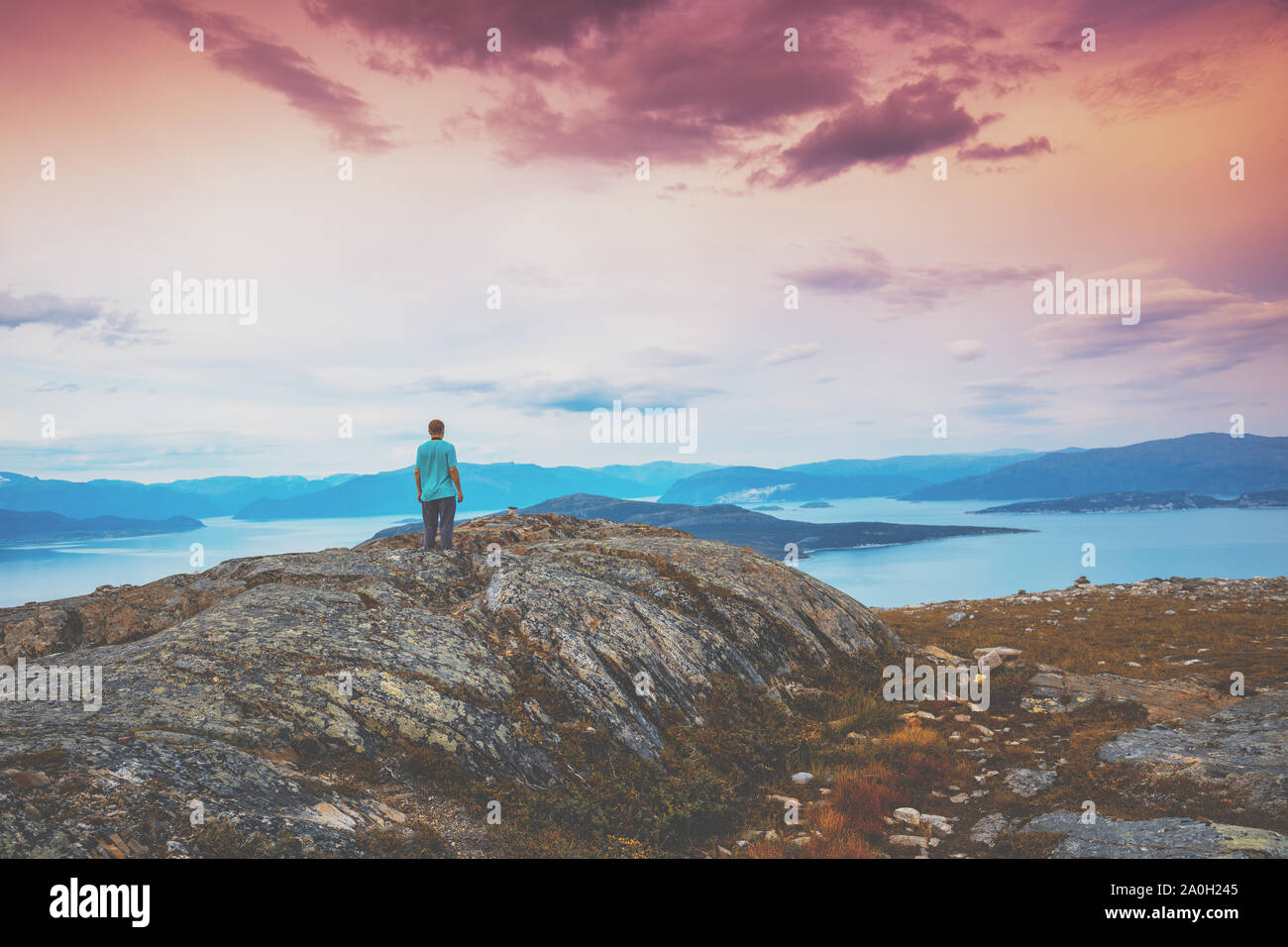 Vue panoramique sur le fjord. Le Crépuscule du temps avec le ciel rose. Le jeune homme debout sur la falaise de roche et regardant la mer. Belle Montagne l Banque D'Images