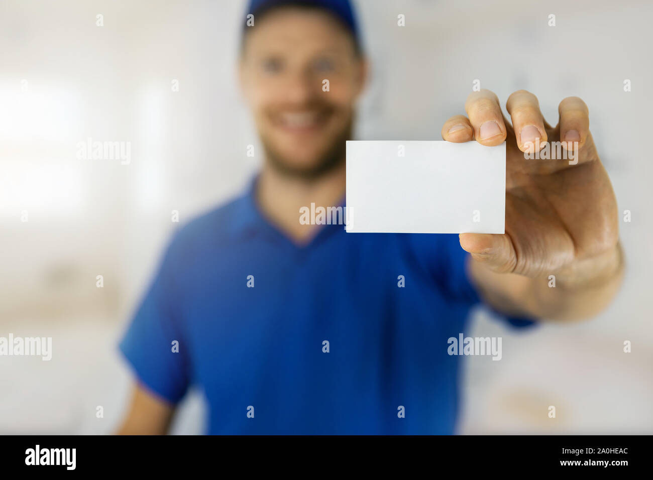 Smiling handyman in blue uniform showing blank business card Banque D'Images