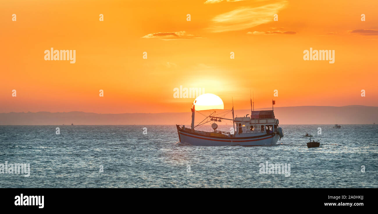 Paysage de la mer au coucher du soleil lorsque les bateaux de pêche en mer de récolter du poisson fin de la journée. Banque D'Images