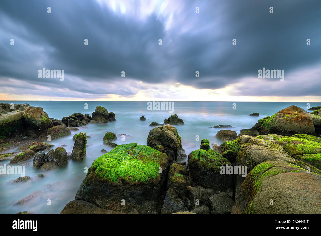 Les algues vertes sur la plage des roches dans l'aube avec ciel dramatique d'accueillir le nouveau jour Banque D'Images