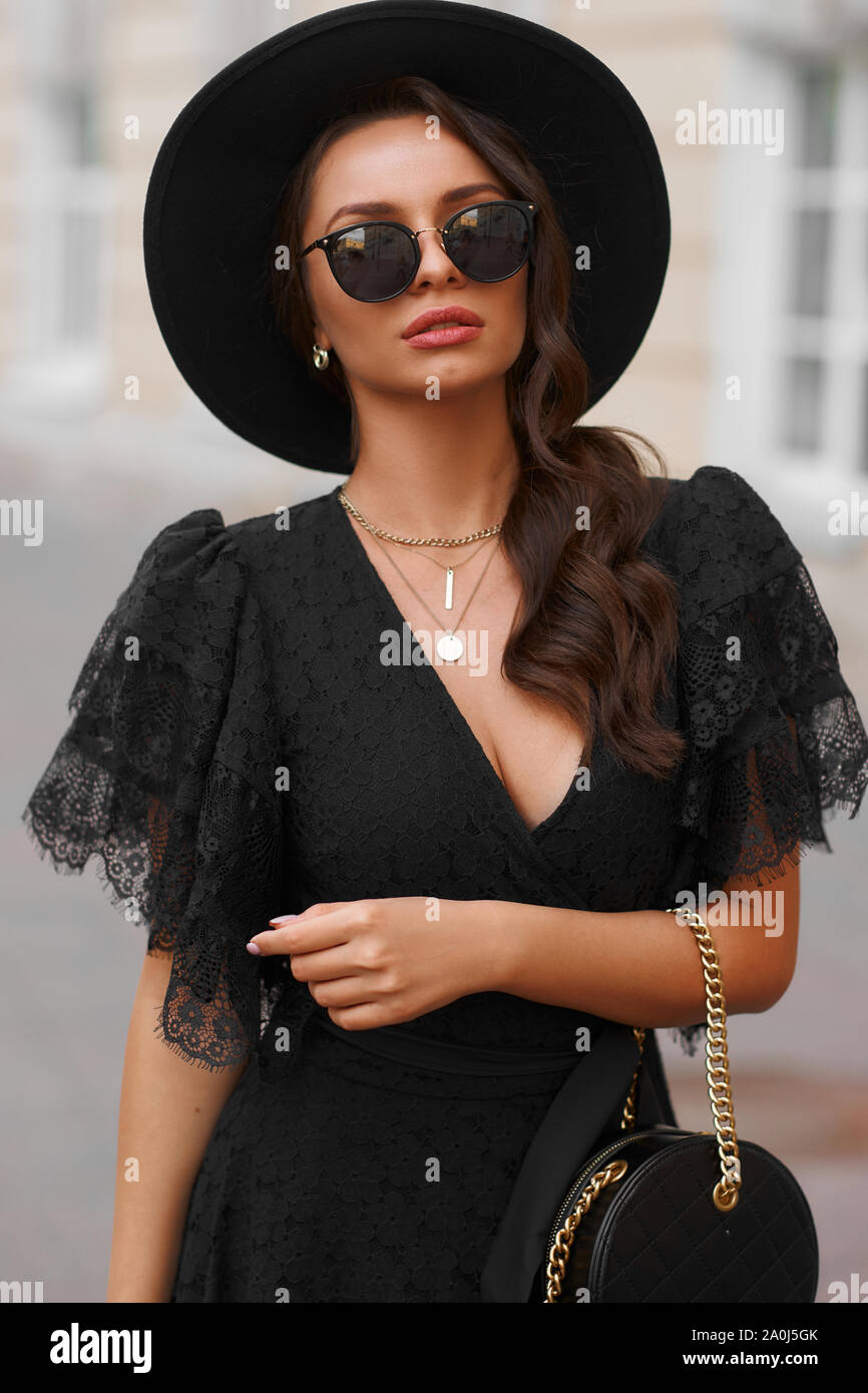 Mode femme élégante au total des vêtements noirs. Jolie fille en robe  noire, un chapeau et des lunettes de soleil et permanent à l'extérieur pose  Photo Stock - Alamy