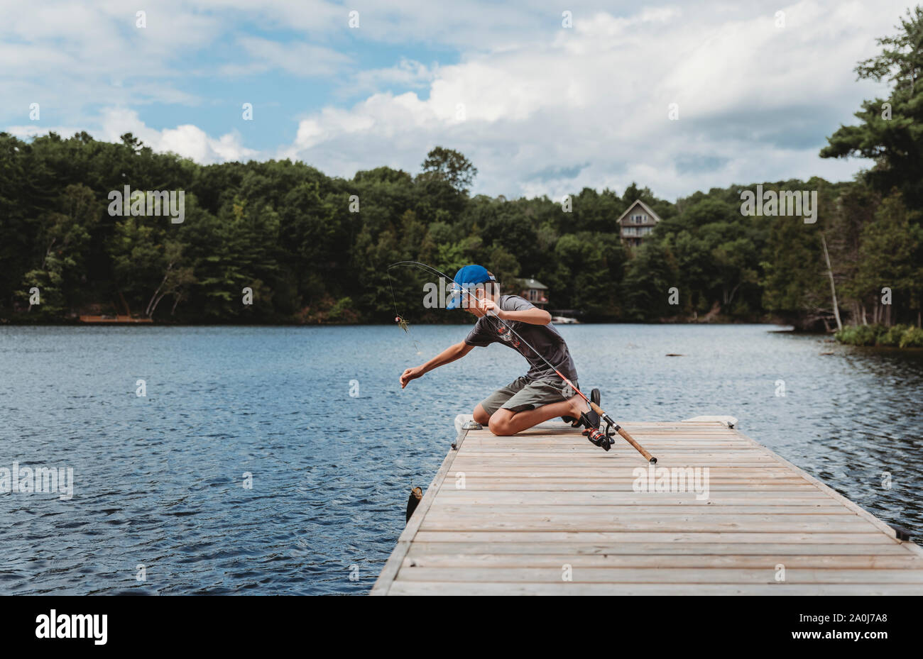 Boy capture d'un poisson avec une canne à pêche sur le bout d'un quai sur un lac. Banque D'Images