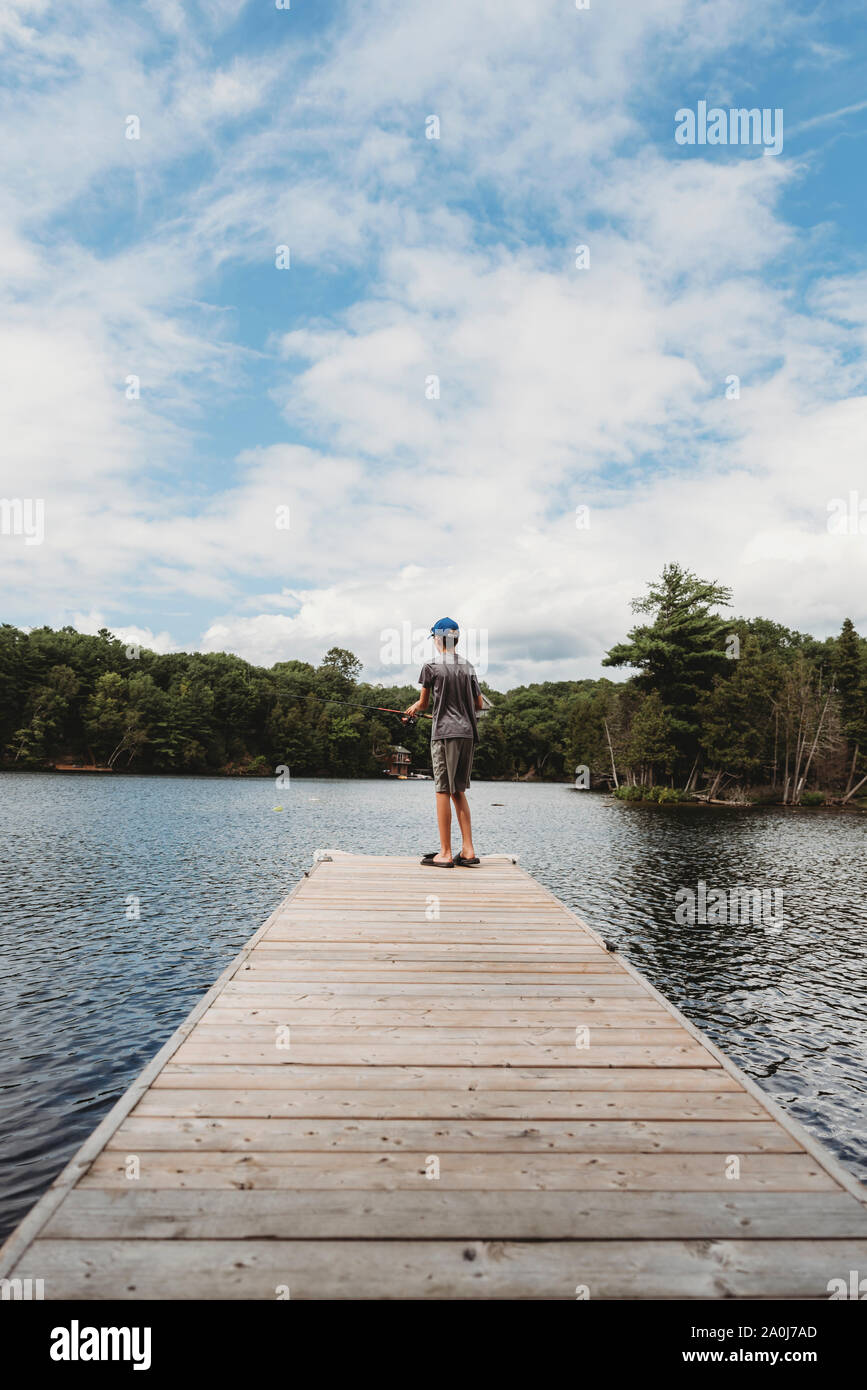Garçon de pêche avec une canne à pêche sur la fin de quai sur un lac en été. Banque D'Images