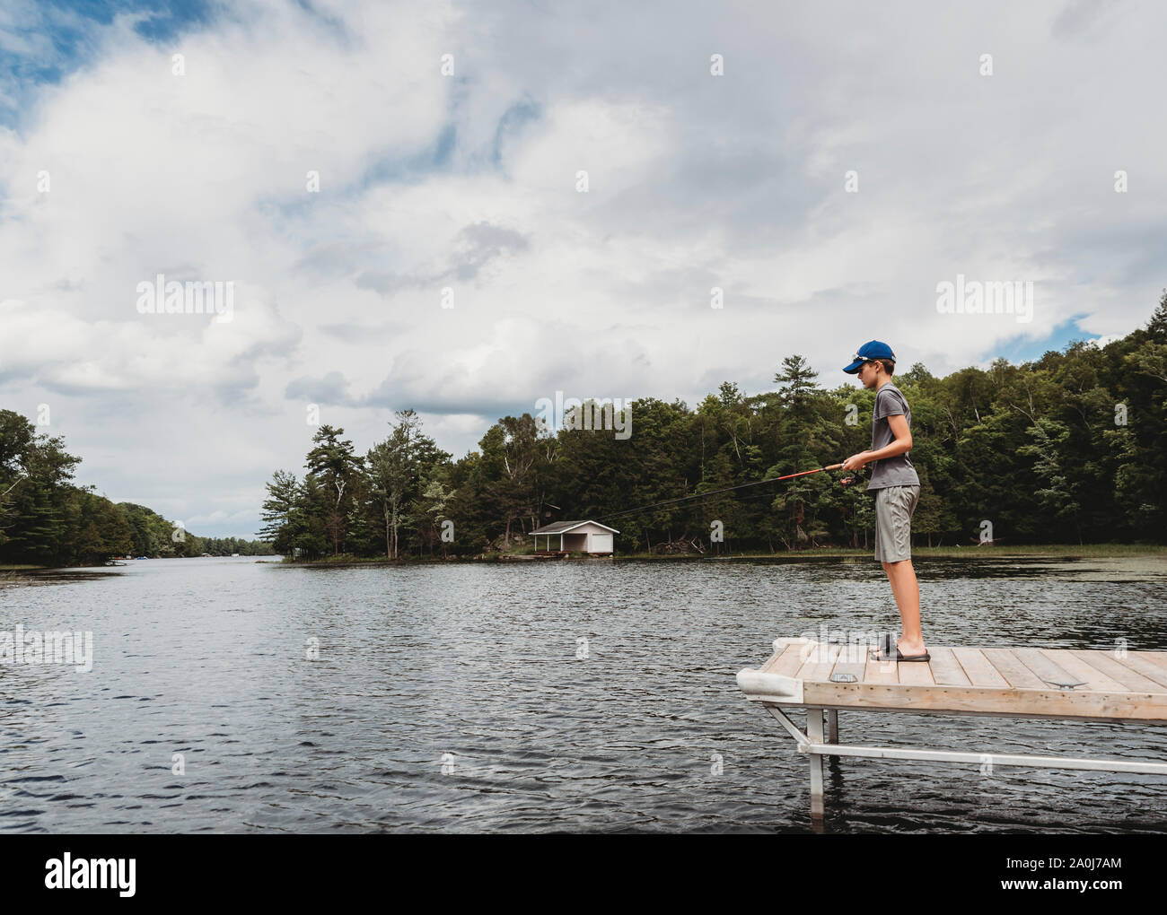 Garçon de pêche avec une canne à pêche sur le bout d'un quai sur le lac en été. Banque D'Images