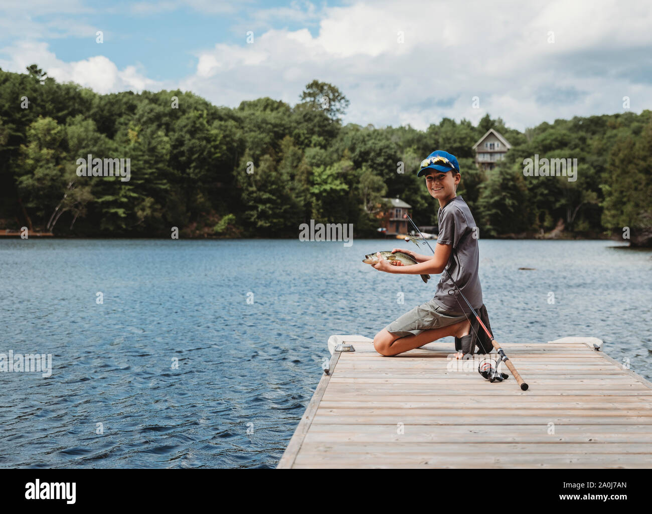 Garçon tenant un poisson qu'il a pris sur le bout d'un quai sur un lac. Banque D'Images