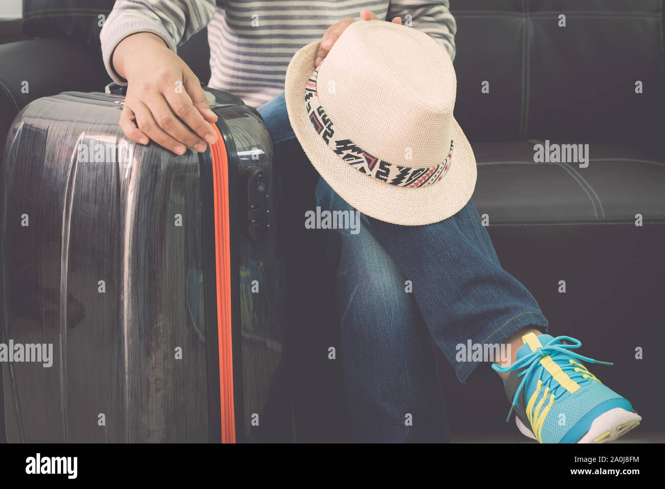 Voyageuses est assis avec sac de voyage et chapeau de paille sur un canapé en cuir à l'aéroport. Concept de voyage. Banque D'Images