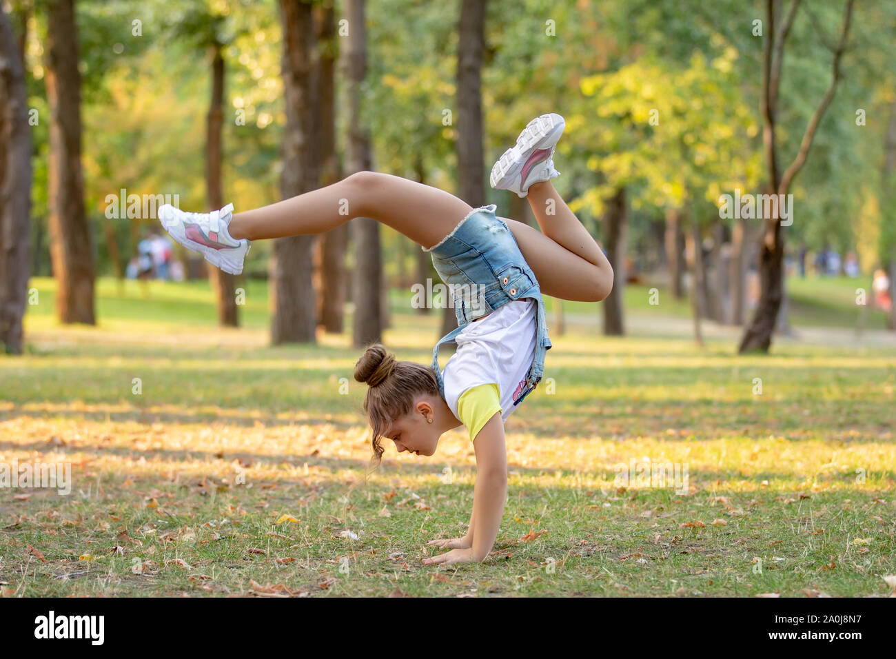 Happy little girl debout sur sa tête sur l'herbe dans le parc. Concept de la petite enfance. Des vacances d'acrobat. Banque D'Images