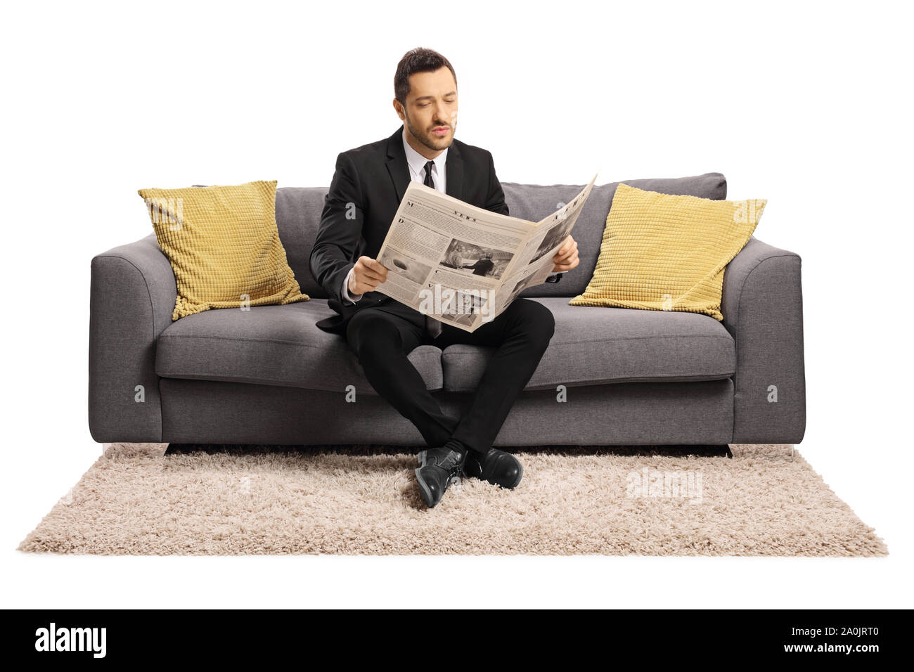 Portrait d'un jeune homme assis sur un canapé et lit un journal isolé sur fond blanc Banque D'Images