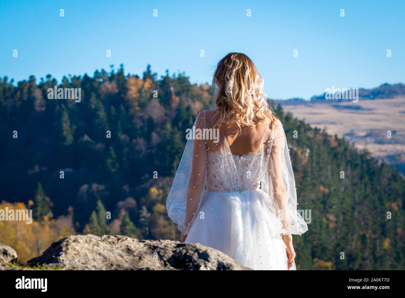 Retour de la mariée en robe blanche debout sur le haut de la montagne, au coucher du soleil. Banque D'Images