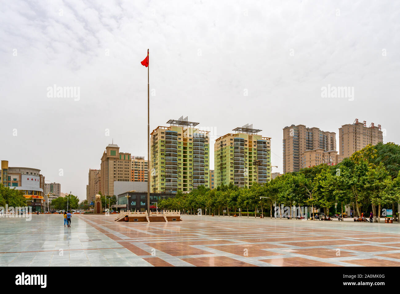 Hotan Tuanjie haut carré en agitant le drapeau chinois avec quelques personnes et les bâtiments résidentiels à l'arrière-plan Banque D'Images
