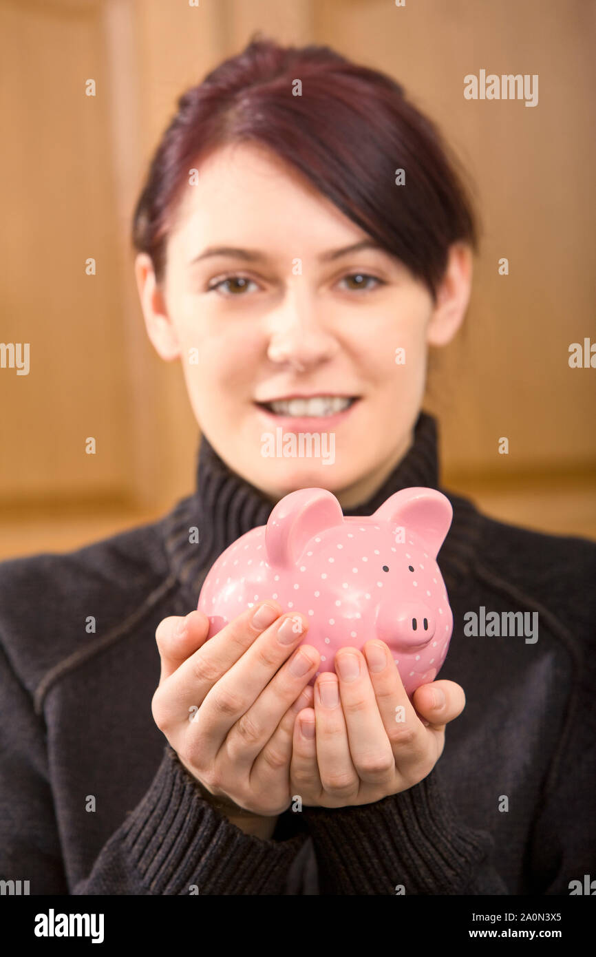 Jeune femme avec ses économies dans un pink piggy bank Banque D'Images