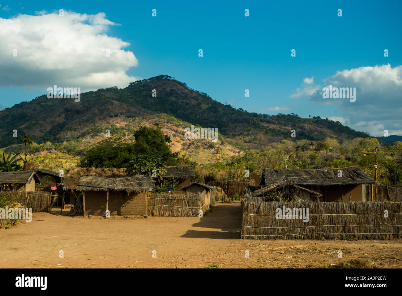 La province de Nampula / Mozambique - 6 juillet 2019 : une route rurale village de huttes de chaume, avec une colline verte à l'arrière-plan sur une journée ensoleillée Banque D'Images