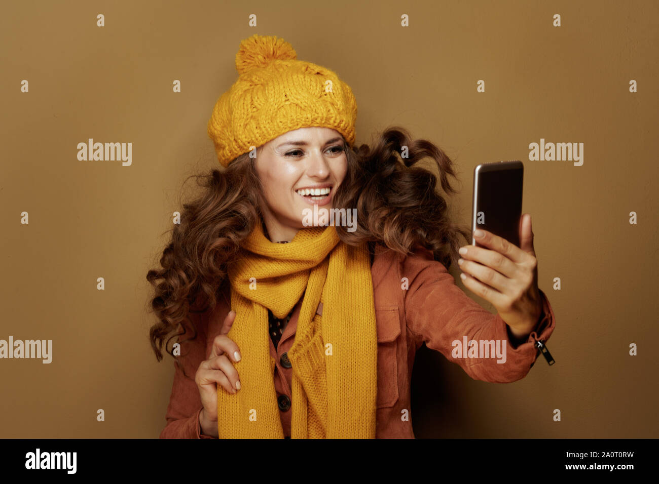 Femme élégante heureux en béret et écharpe jaune en tenant avec téléphone et selfies isolé sur beige. Banque D'Images