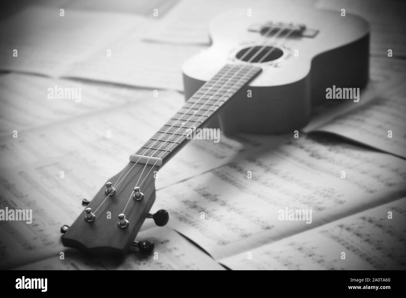 Une image noir et blanc d'un ukulélé allongé sur des feuilles avec des notes de musique laissé par le compositeur. Banque D'Images
