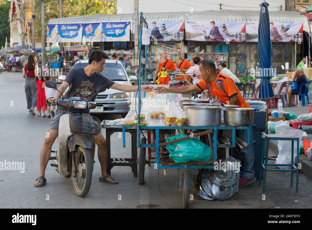 SUKHOTHAI, THAÏLANDE - 25 décembre 2018 : Le jeune homme thaï sur le scooter paie la nourriture au vendeur de rue Banque D'Images