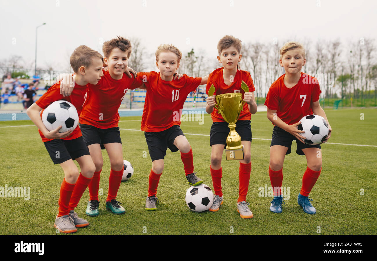 Heureux de l'équipe de sports Junior. Les jeunes garçons dans l'équipe de soccer Holding Golden Cup et des ballons de football. Groupe d'enfants de l'école gagnante du Tournoi sportif. Les écoles F Banque D'Images