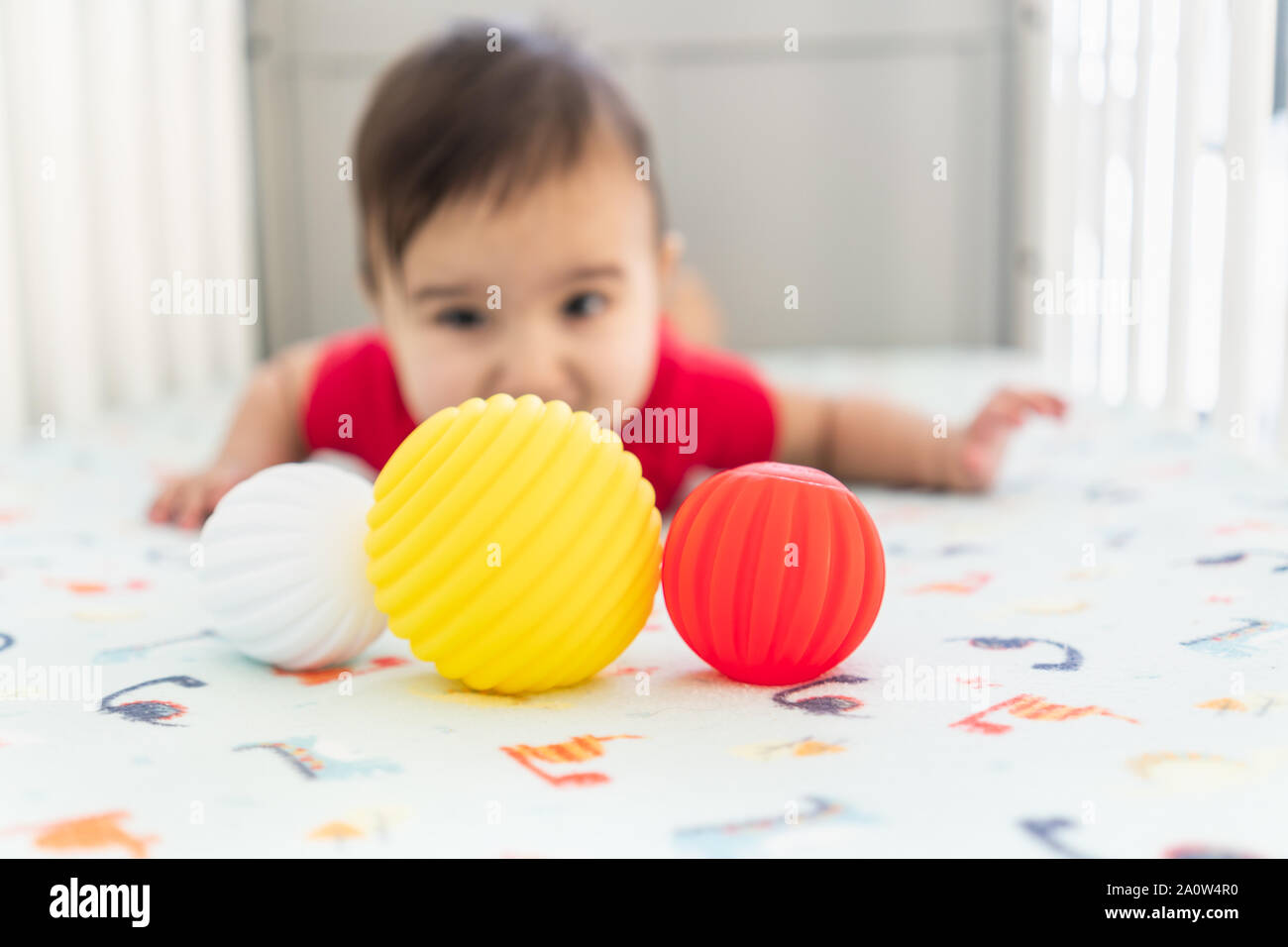 Bebe Jouant Avec Des Balles En Caoutchouc Jouets Dans Le Lit Dans Une Salle Lumineuse Enfant Portant Une Robe Rouge Portant Sur La Feuille De Huche De Dinosaure Ludique Photo Stock
