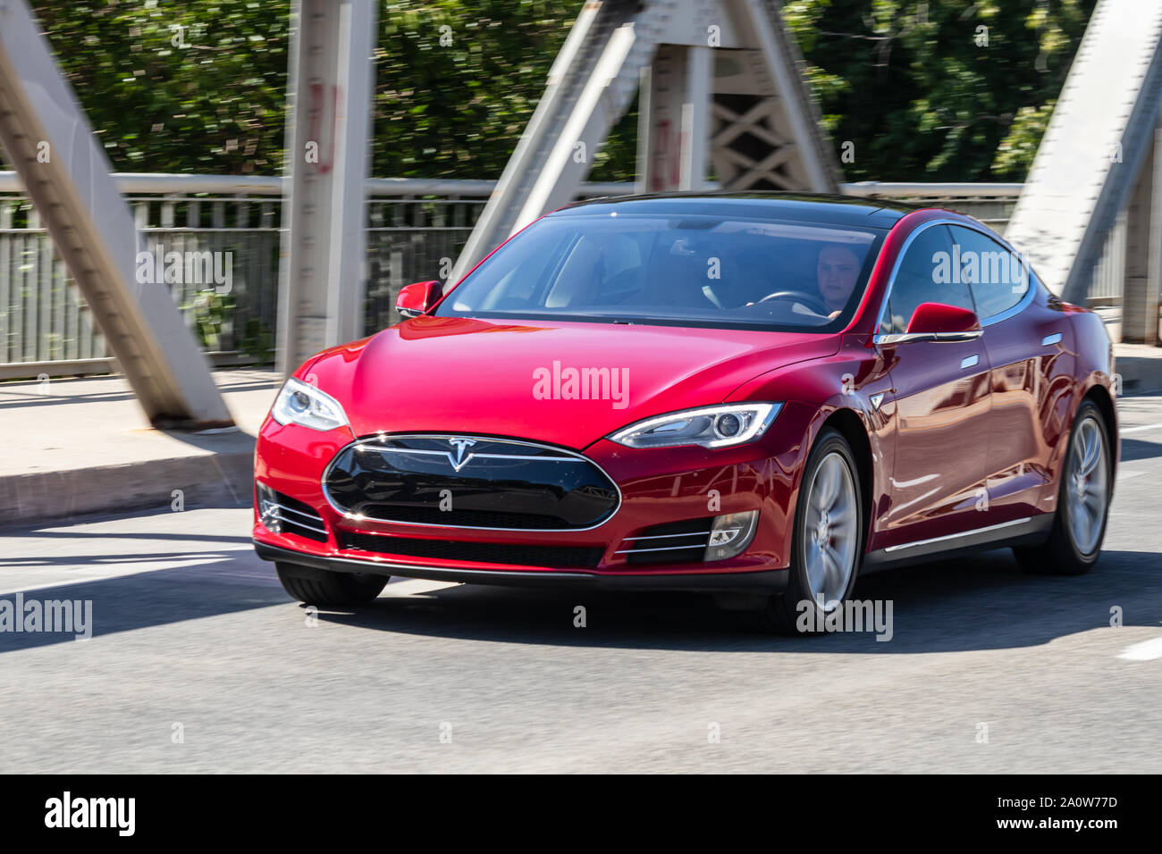 Homme conduisant une voiture électrique, une Tesla Model S sur une journée ensoleillée. Banque D'Images