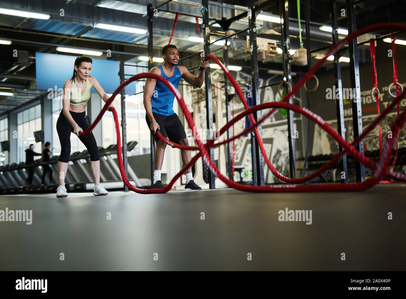 Portrait de grand angle fit young couple exercising avec cordes bataille au cours de la force d'entraînement dans la salle de sport fonctionnelle, copy space Banque D'Images