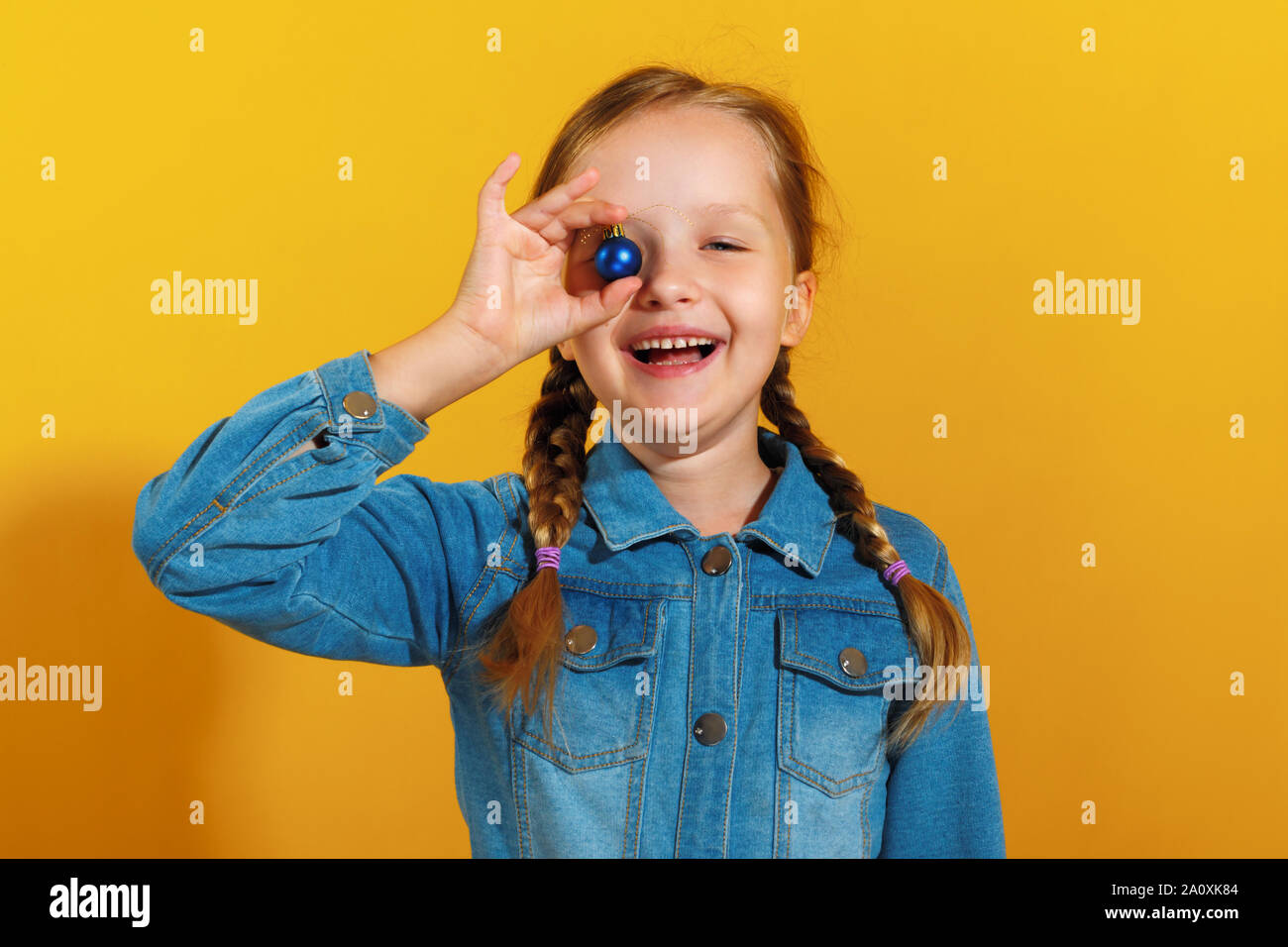 Petite fille joyeuse avec une boule de noël jouet sur un fond jaune. Le concept de Noël, nouvel an. Banque D'Images