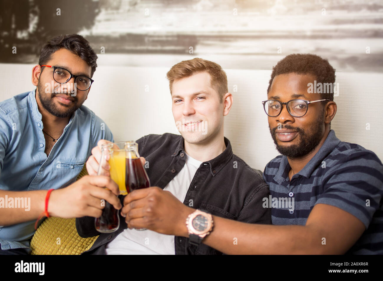 Closeup portrait de trois beaux mâles multi ethnic friends en tenues décontractées tintement des bouteilles de boissons smiling at camera. Les gens, hommes, leis Banque D'Images