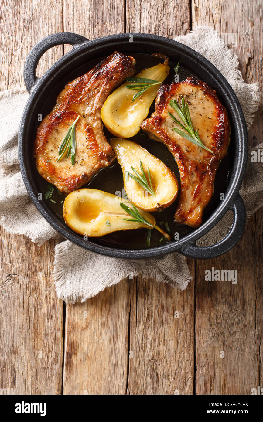 Les aliments d'automne côtelettes de porc aux poires cuites avec nervures et romarin en sauce au miel dans une casserole sur la table. Haut Vertical Vue de dessus Banque D'Images