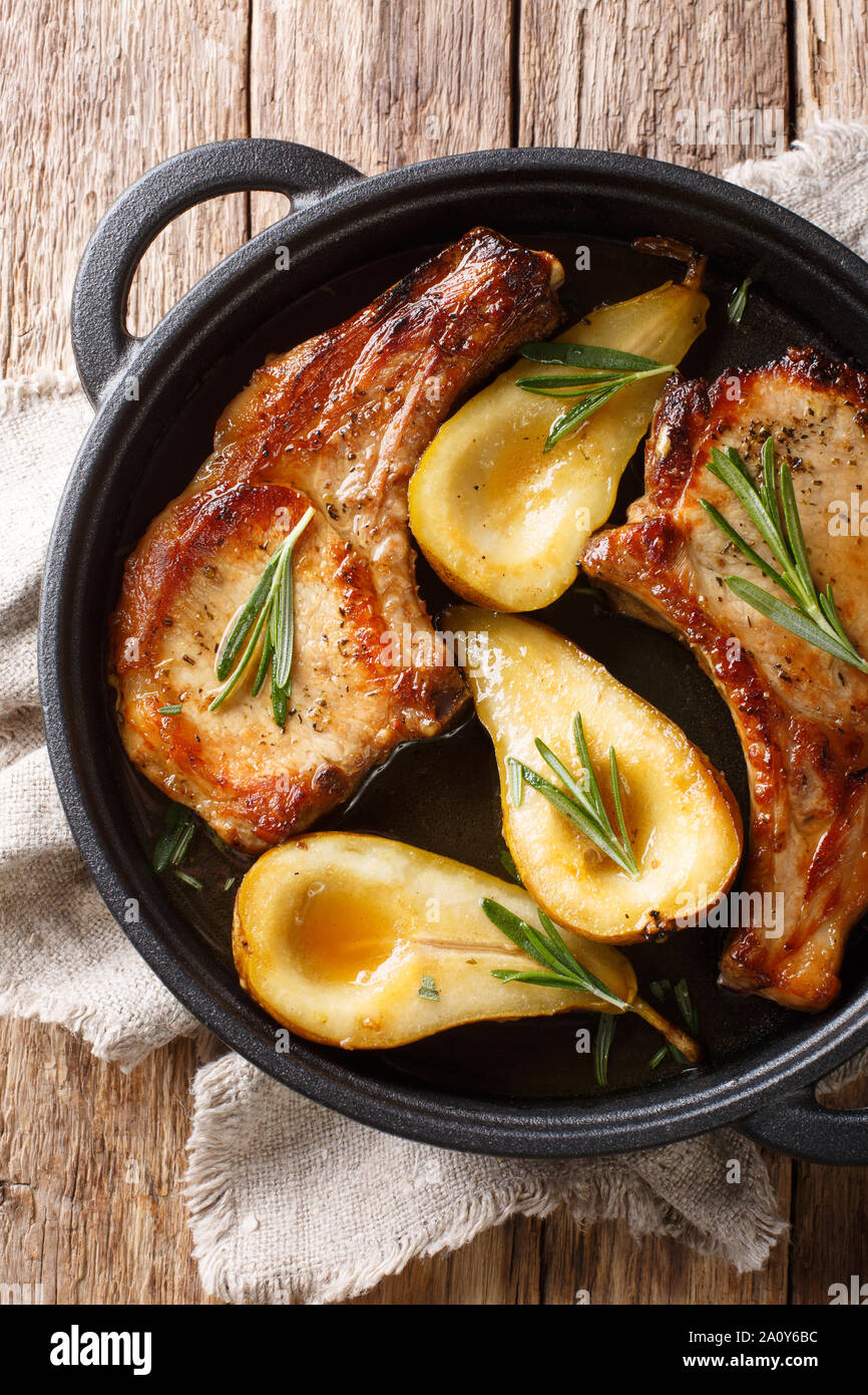 Côtelettes de porc cuit chaud savoureux aux poires et romarin en sauce au miel dans une casserole sur la table. Haut Vertical Vue de dessus Banque D'Images