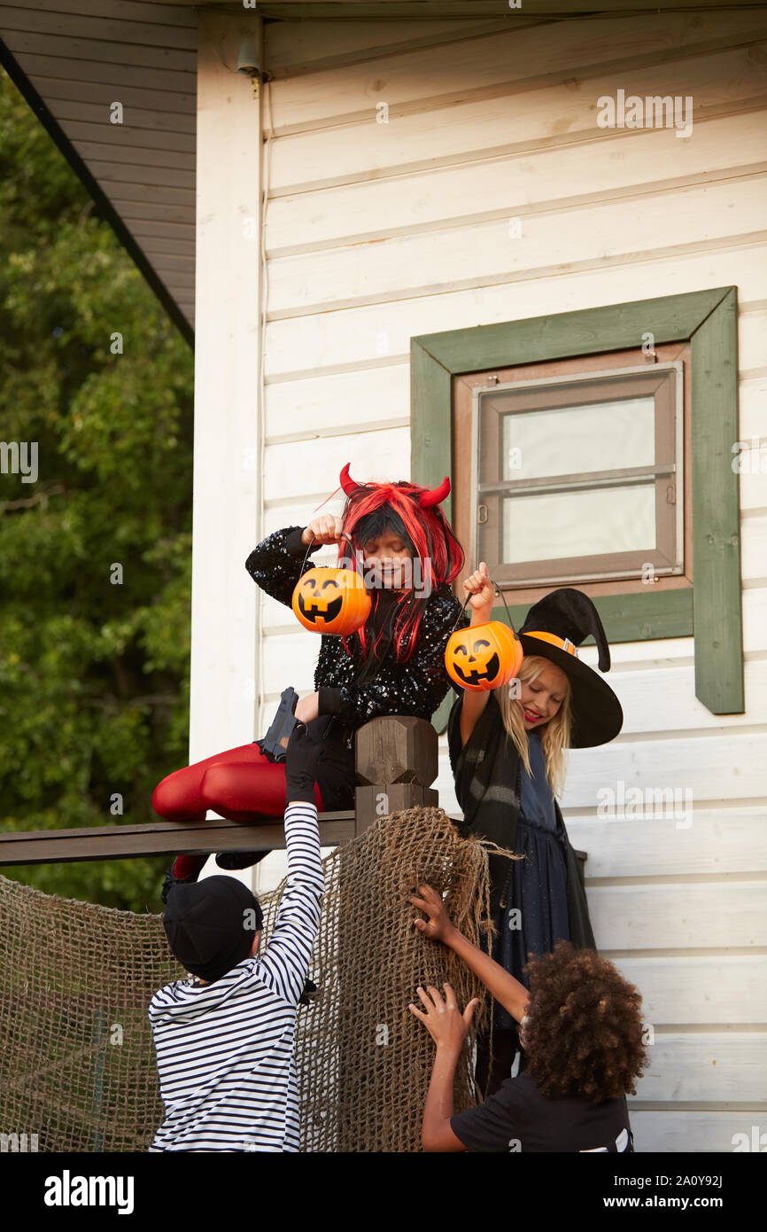 Groupe de quatre enfants sournois grimpe sur la clôture pendant que des friandises à l'Halloween, copy space Banque D'Images