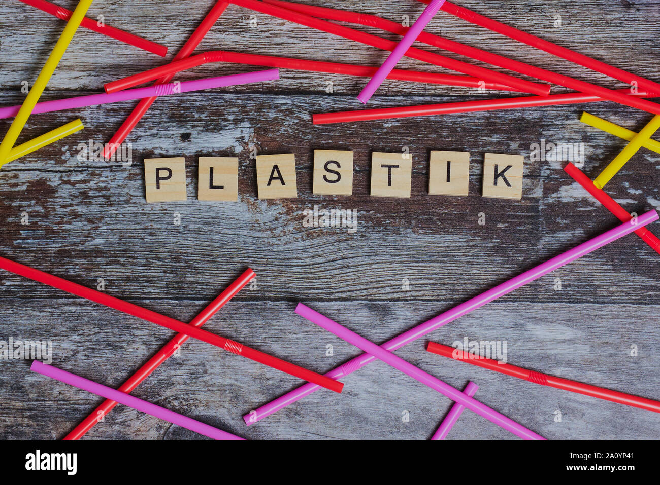 Le mot allemand pour le plastique jeté avec des lettres sur un fond de bois à côté des pailles de couleur Banque D'Images