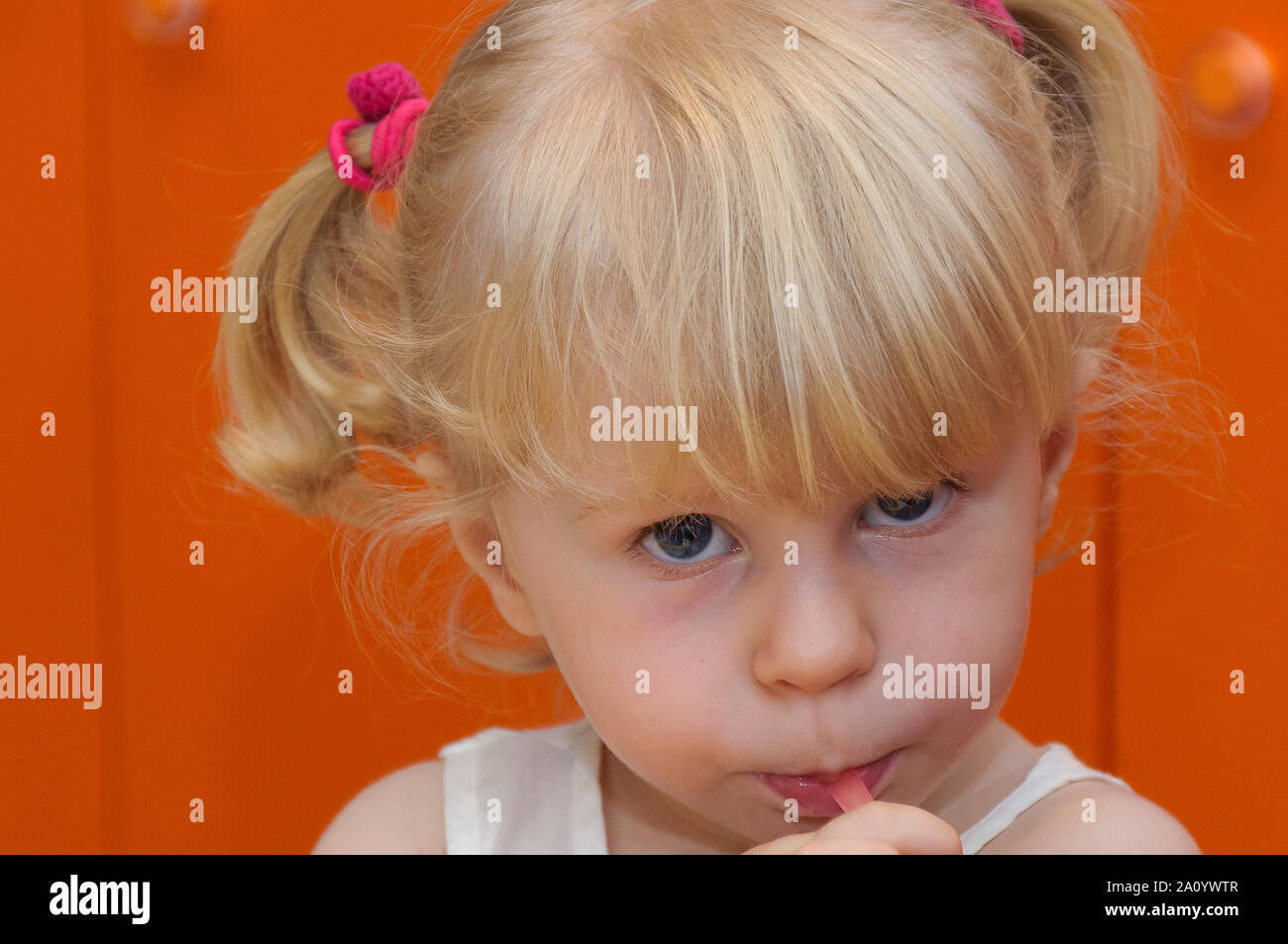 Gros plan portrait d'une adorable jolie mignonne petite fille de deux ans de cheveux blonds vieux avec les yeux bleus et des queues de cochon avec de la paille rose. Banque D'Images
