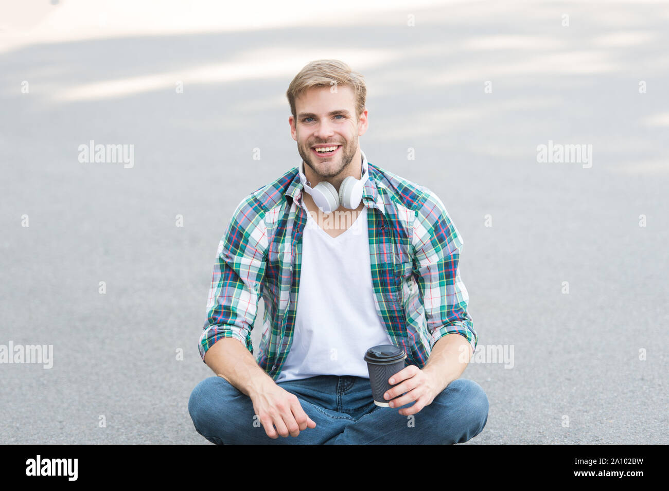 Être gai. chemise à carreaux homme étudiant. Se détendre et recharger. café d'aller. guy boire un café en plein air. L'homme s'asseoir sur le sol. étudiant insouciant en casque. l'éducation en ligne. écouter la musique. ebook concept. Banque D'Images