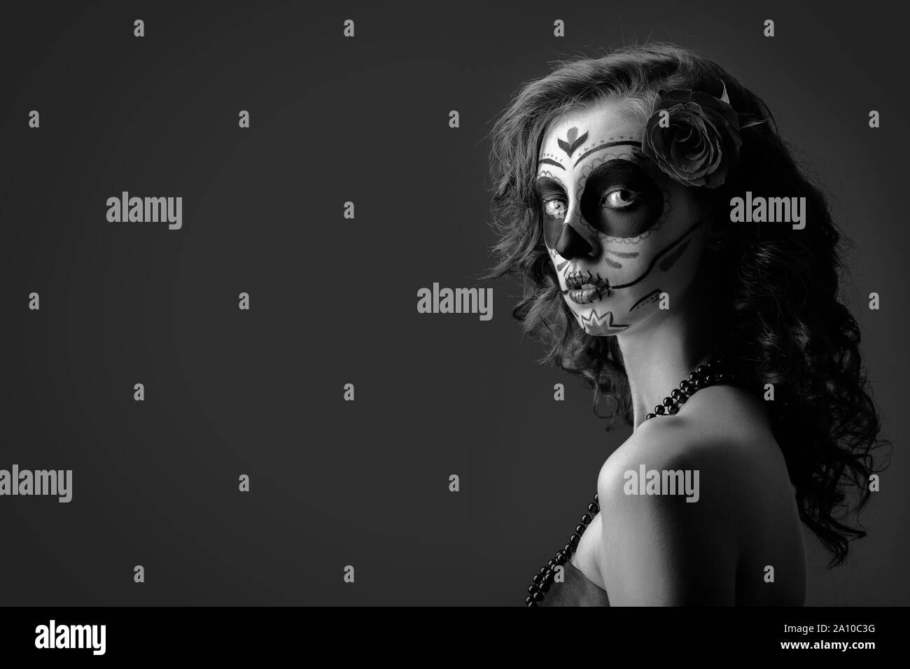 Jeune femme avec santa muerte maquillage sur fond sombre avec copie espace looking at camera, monochrome Banque D'Images