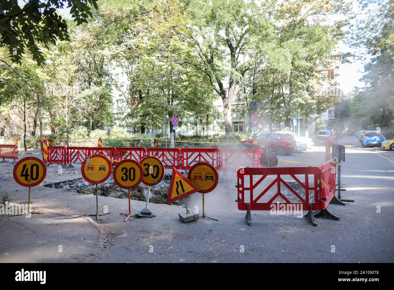 Panneaux d'avertissement de trafic routier et d'une bordure en plastique autour d'un grand trou dans l'asphalte d'où sort la vapeur Banque D'Images