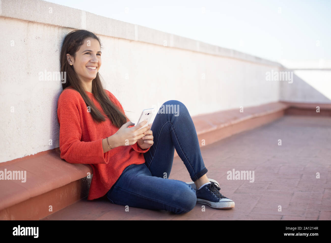 Chica adolescente sonriente mirando el sentada smartphone en la azotea Banque D'Images