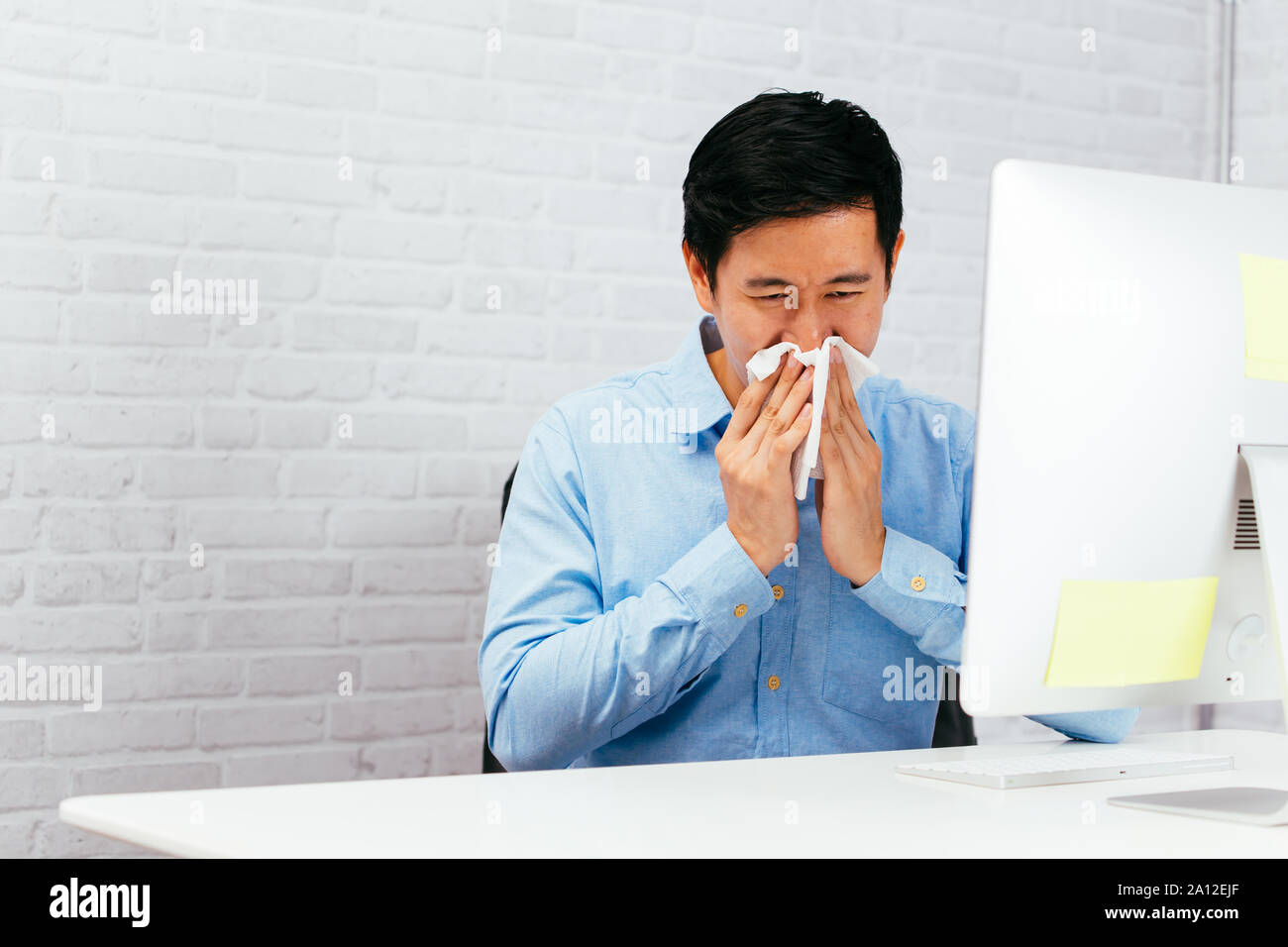 Entrepreneur mâle malade l'éternuement avec nappes à l'office de tourisme avec l'exemplaire de l'espace. Jeune homme asiatique avec la maladie et à l'allergie Banque D'Images