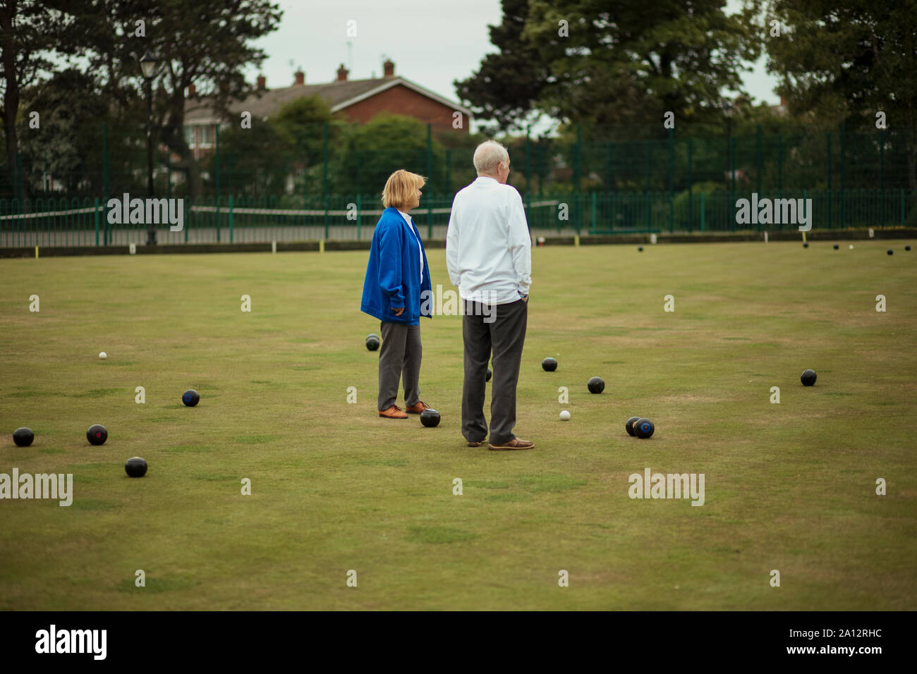 Deux adultes se tenant ensemble au milieu d'un terrain de boules, entouré de boules de pétanque. Banque D'Images