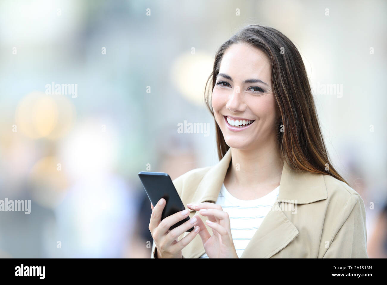 Femme heureuse est titulaire d'un téléphone intelligent à la caméra au comité permanent dans la rue Banque D'Images