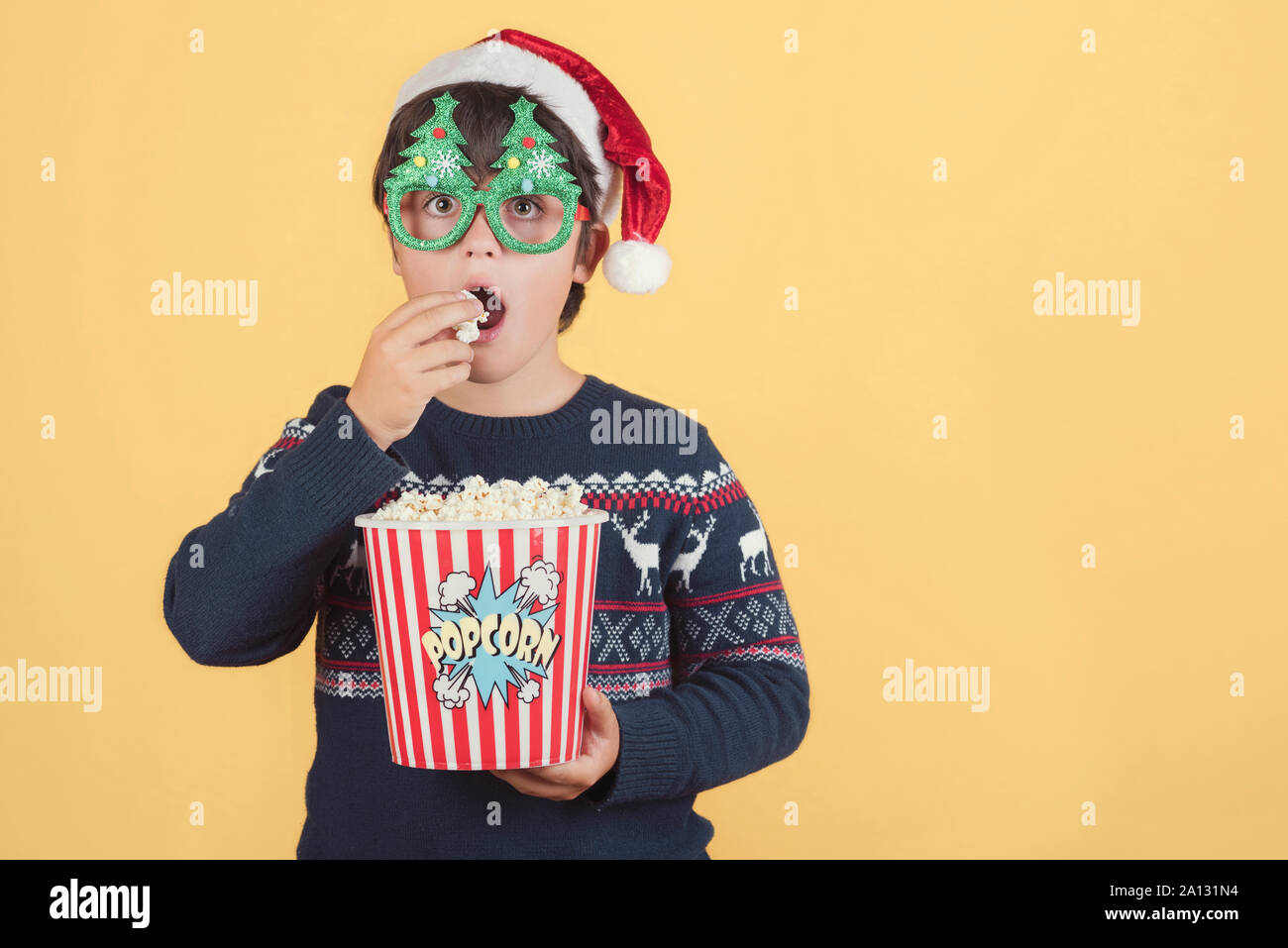 Surpris child Wearing Christmas Hat with popcorn sur fond jaune Banque D'Images