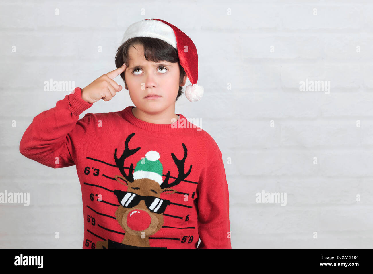 Thoughtful child Wearing Christmas Santa Claus Hat sur fond brique Banque D'Images