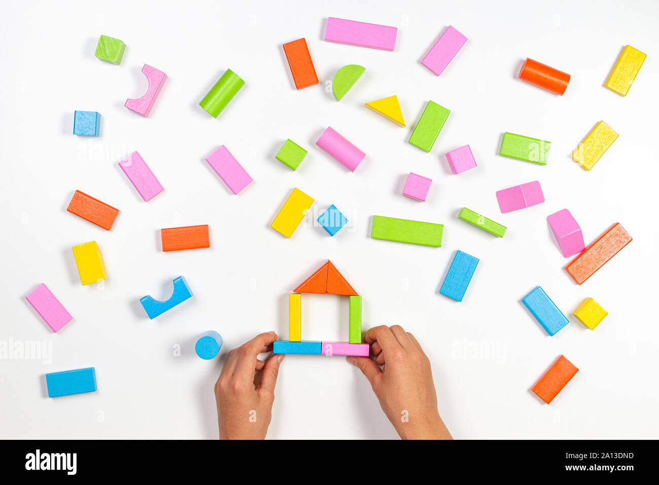 Kid mains jouant avec blocs de construction en bois coloré sur fond de table blanc. Vue d'en haut Banque D'Images