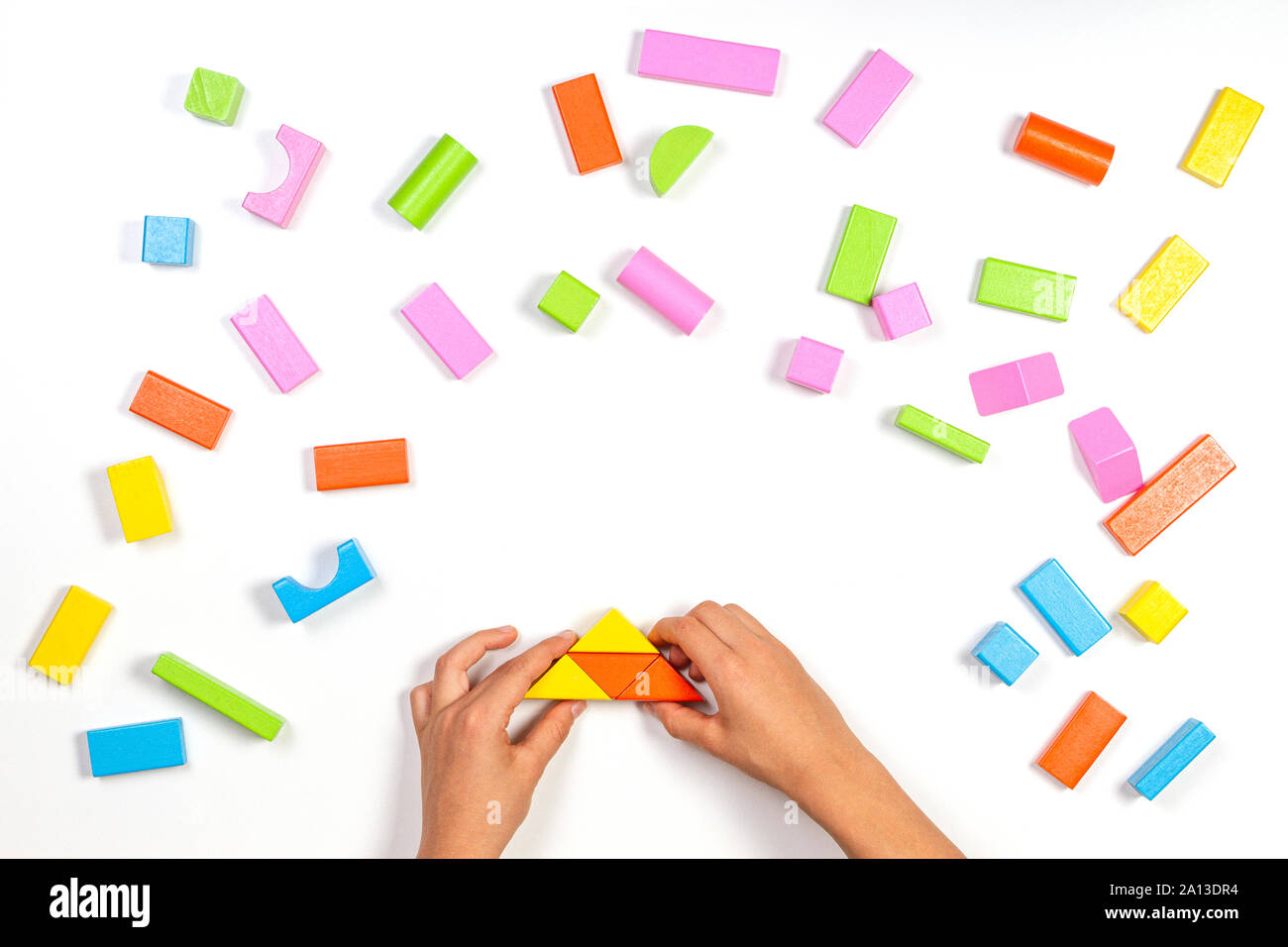 Kid mains jouant avec blocs de construction en bois coloré sur fond de table blanc. Vue d'en haut Banque D'Images
